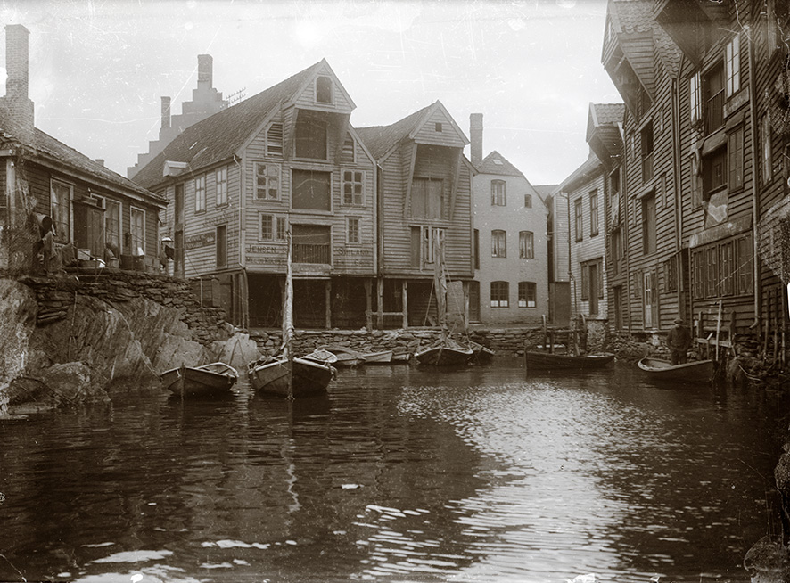 Til venstre, tollpakkhuset på Kjeringholmen. I midten, sjøhusene over det gjenfylte sundet mellom Holmen og Østervåg. Til høyre, sjøhusrekken mot Soilandsbryggen. Ca 1900. Fotograf: Eide, Waldemar (1886-1963). Byarkivets fotosamling.